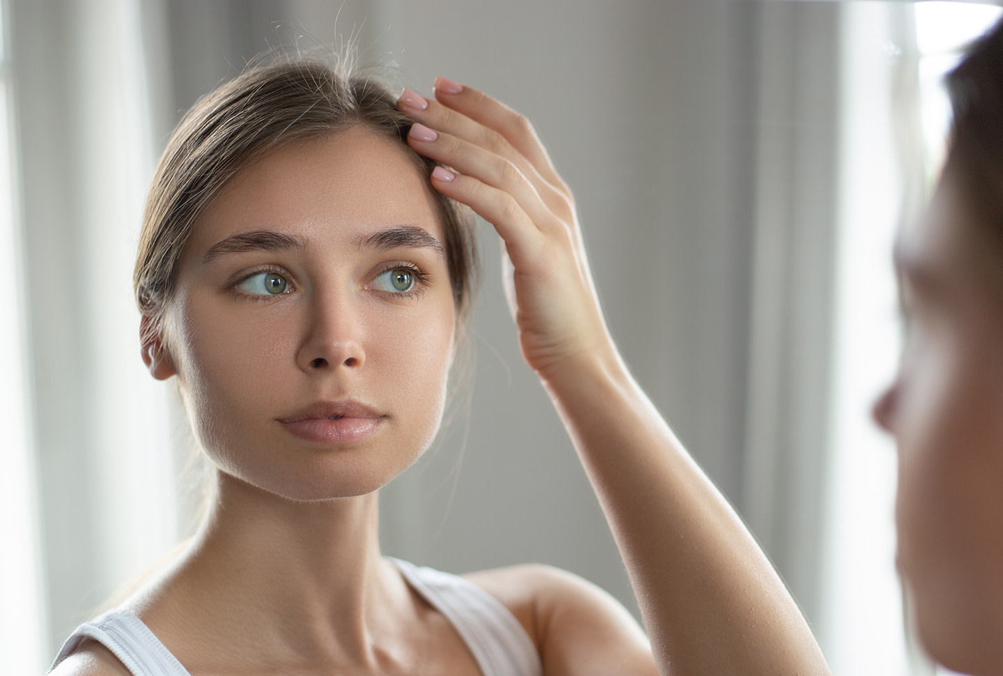 Una niña inspecciona el contorno del cuero cabelludo con su mano frente al espejo para detectar si hay caspa. Una niña inspecciona el contorno del cuero cabelludo con su mano frente al espejo para detectar si hay caspa.