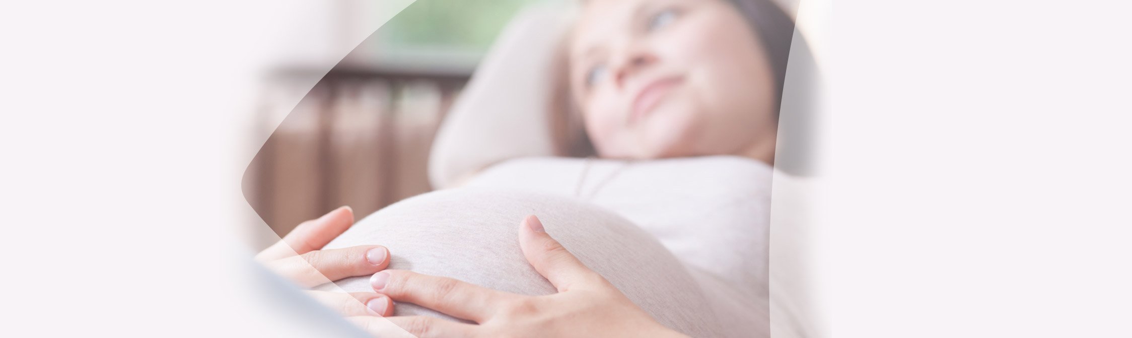 Schwangere Frau liegt auf der Couch und fasst sich an den Bauch