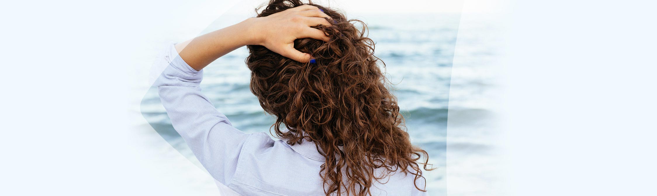 Frau greift sich in die Haare und schaut aufs Meer hinaus