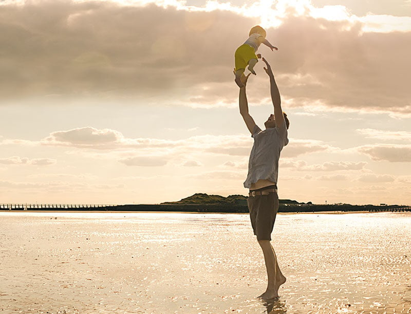 Mann spielt mit Kind am Strand