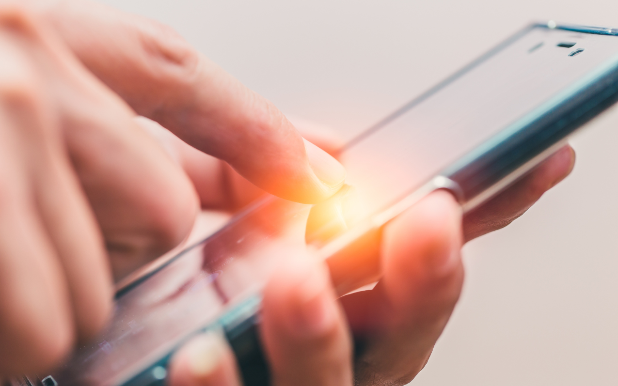 Close-up of a finger tapping a smartphone touchscreen with a glowing light effect at the point of touch.