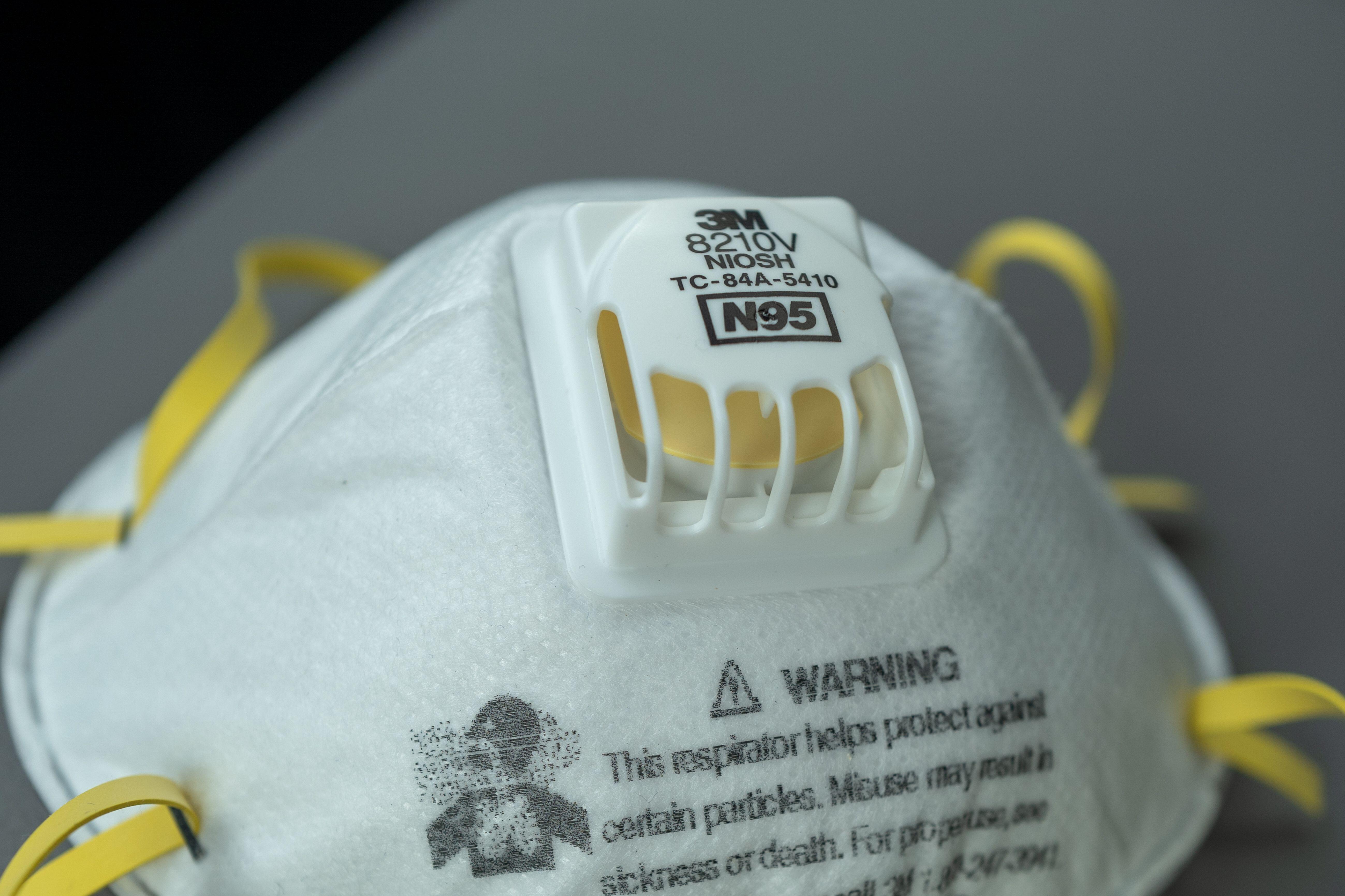 3M white N95 respirator mask with yellow straps and exhalation valve, showing NIOSH certification markings