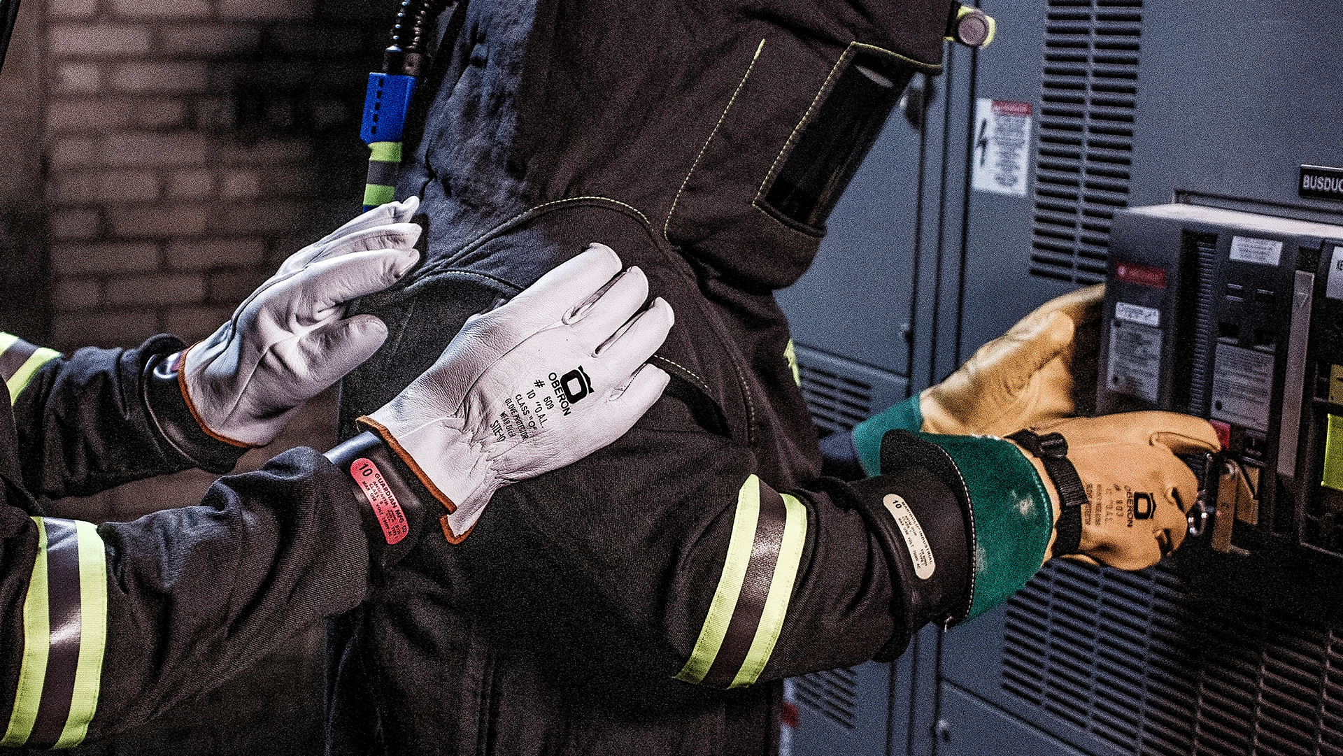 Worker wearing white and tan work gloves performing electrical maintenance on industrial equipment with safety gear visible.