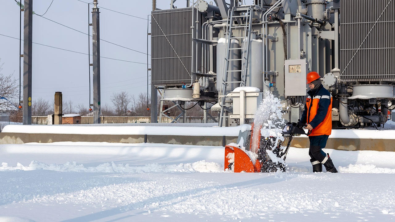 A man with a snowplow is working and removing the snow. On the territory of the electrical substation.