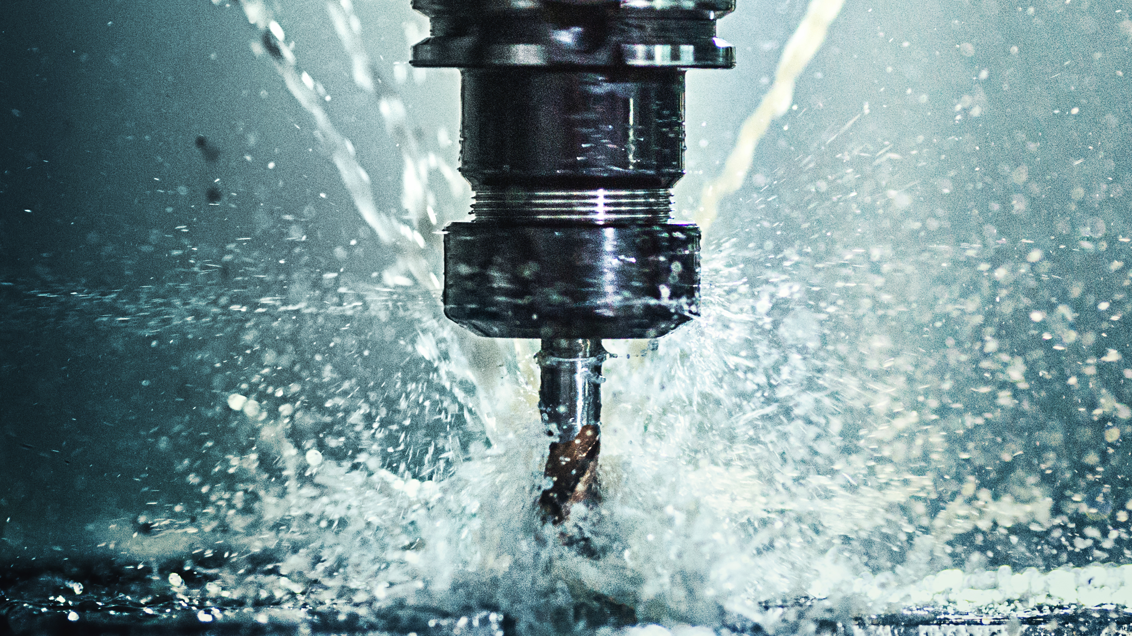 CNC milling machine cutting metal with coolant spray creating dramatic water droplets in industrial manufacturing setting.