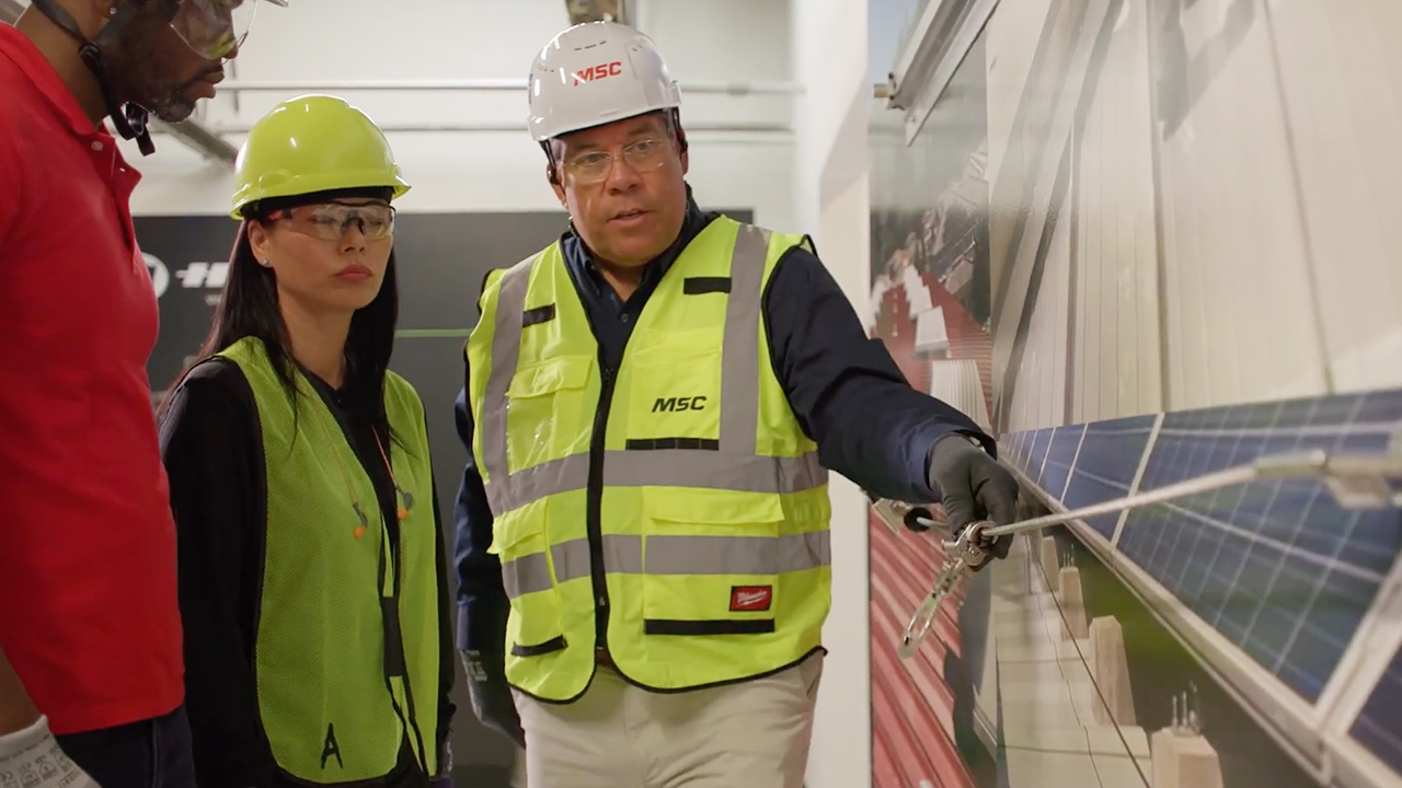 Three workers in safety gear and yellow vests examining solar panels in an industrial facility