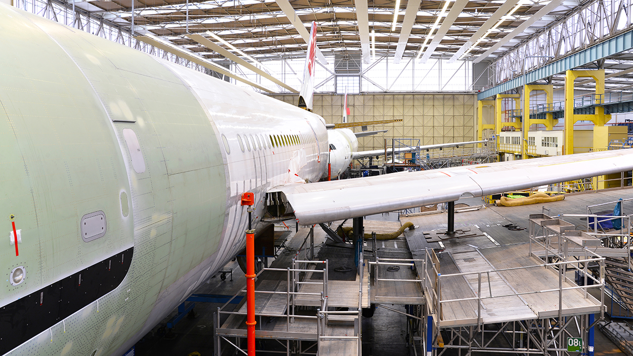 Aircraft fuselage and wing under assembly in large industrial hangar with yellow equipment