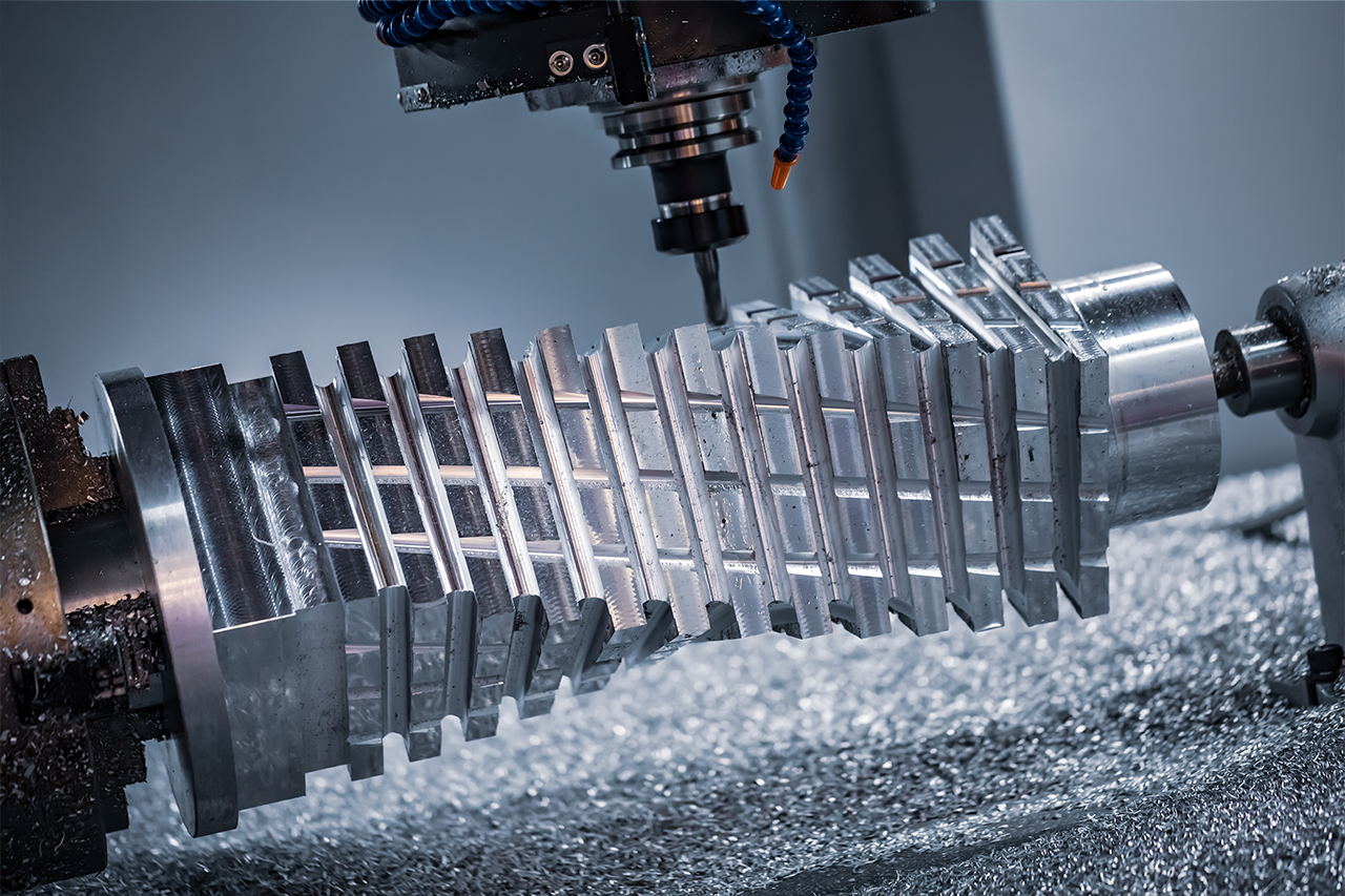 CNC milling machine cutting a large metallic gear shaft with precision grooves, metal shavings visible on work surface.