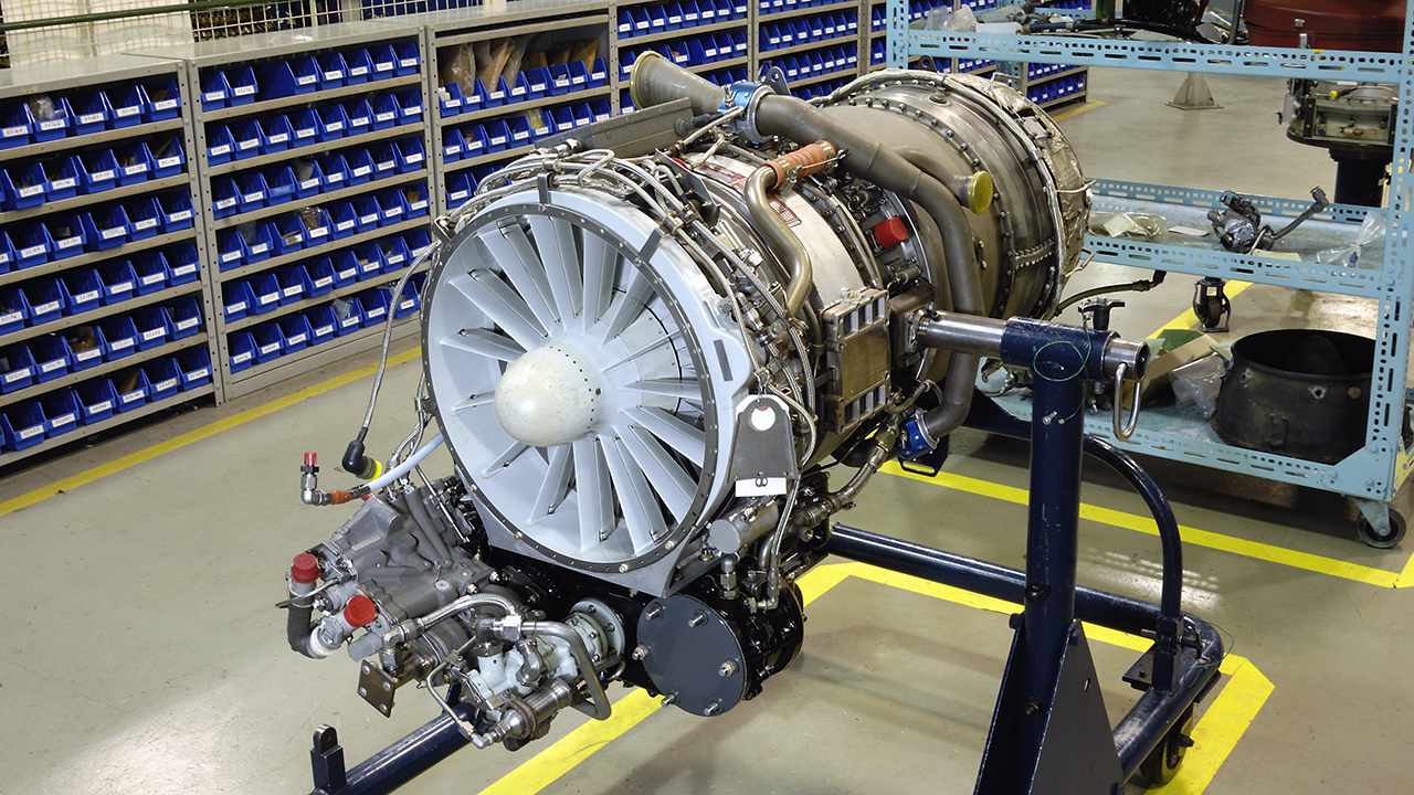 Aircraft jet engine on maintenance stand in warehouse with blue storage bins on shelves in background.