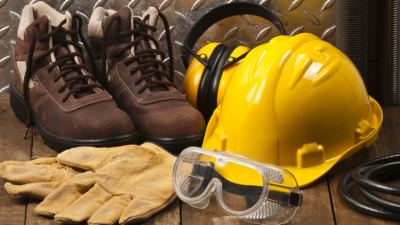 Construction safety equipment including brown work boots, yellow hard hat with ear protection, safety goggles, and work gloves.