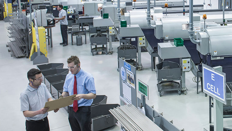 Two workers reviewing clipboard in modern manufacturing facility with industrial machinery and equipment
