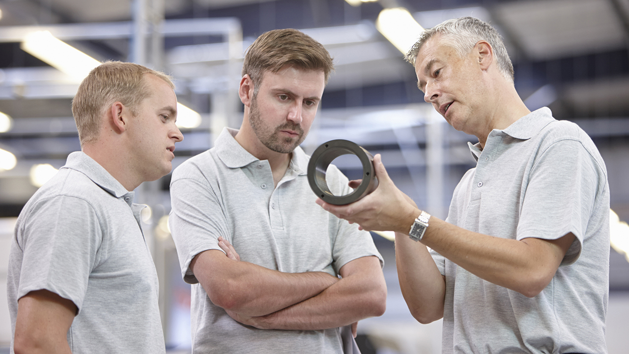 Three men looking at and discussing a metal part one of them is holding
