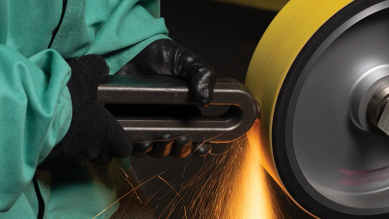 Worker in green jacket and black gloves using angle grinder on metal, creating orange sparks