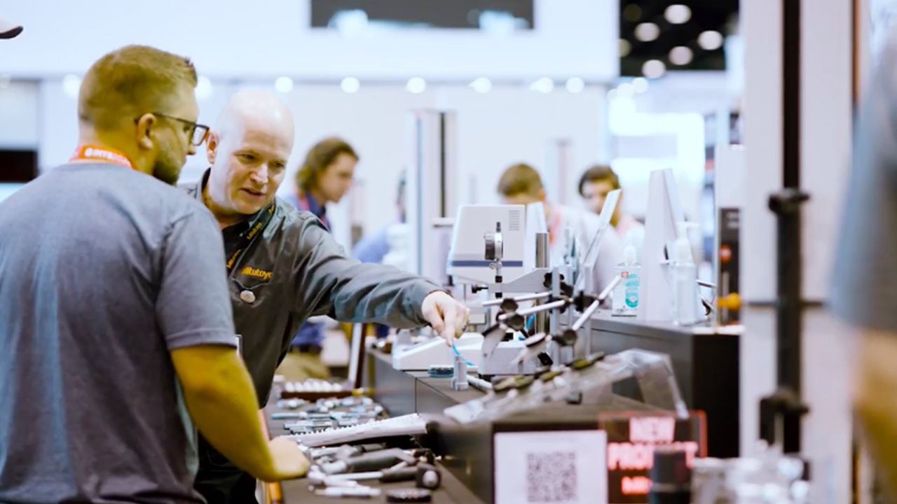 Two professionals examining industrial tools and equipment at a trade show booth display table.