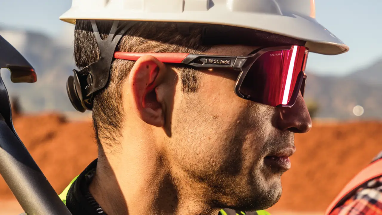 Worker wearing white hard hat and red safety glasses with dark lenses at outdoor construction site