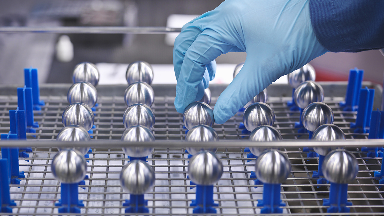 Hand in blue glove placing metallic spherical molds on blue rack in pharmaceutical manufacturing facility