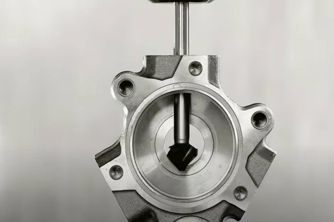 Close-up of a metallic engine valve component with a piston rod inserted through a circular chamber with bolt holes.