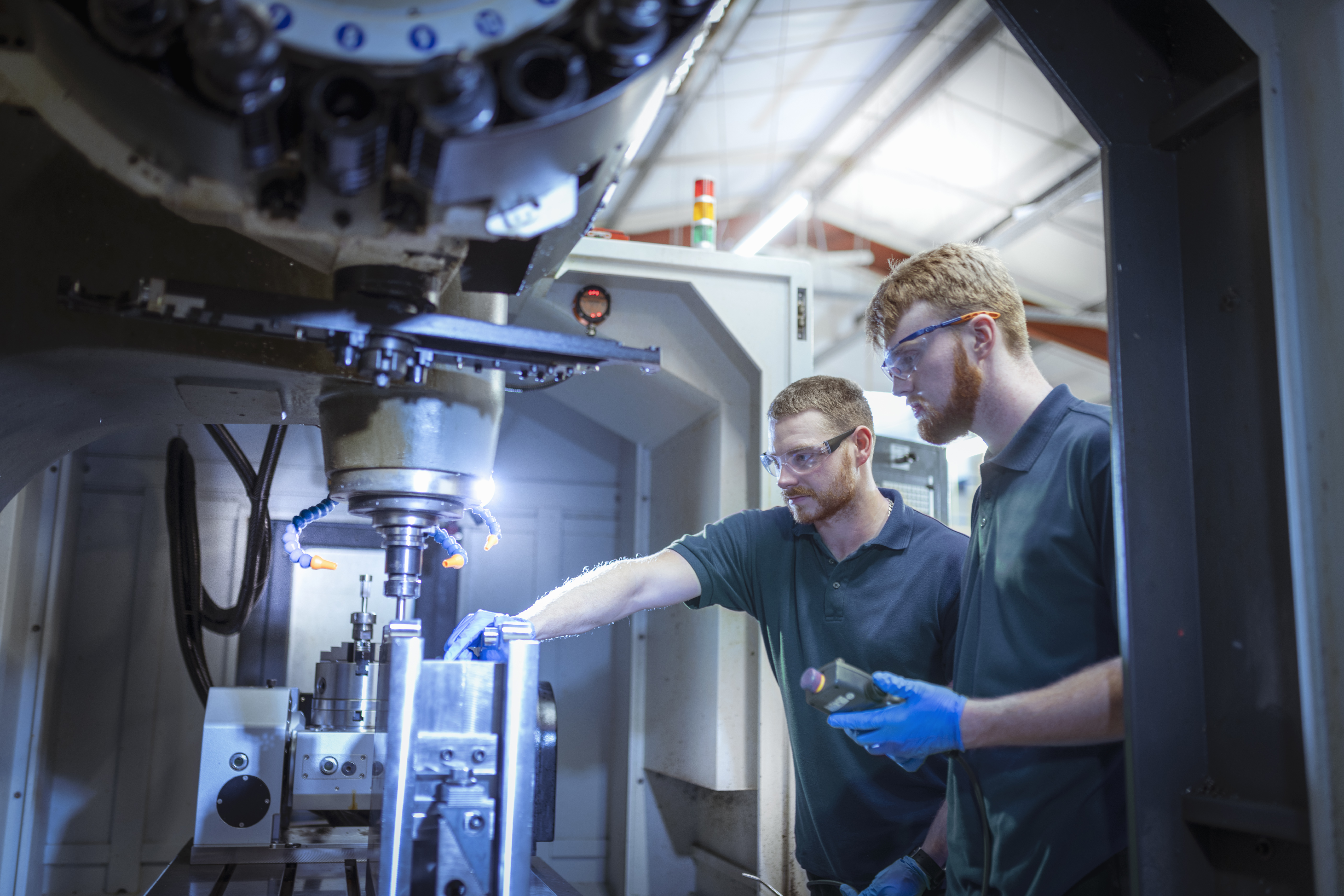 Two workers in safety glasses operating a machine in an industrial manufacturing facility.