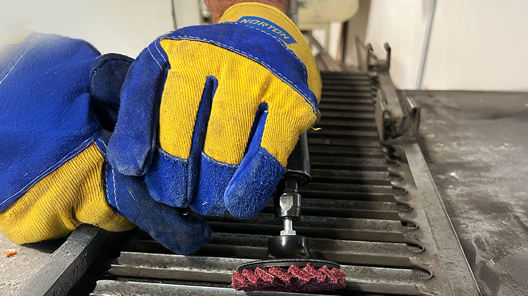 Blue and yellow gloved hands holding a tool with a mini flap disc