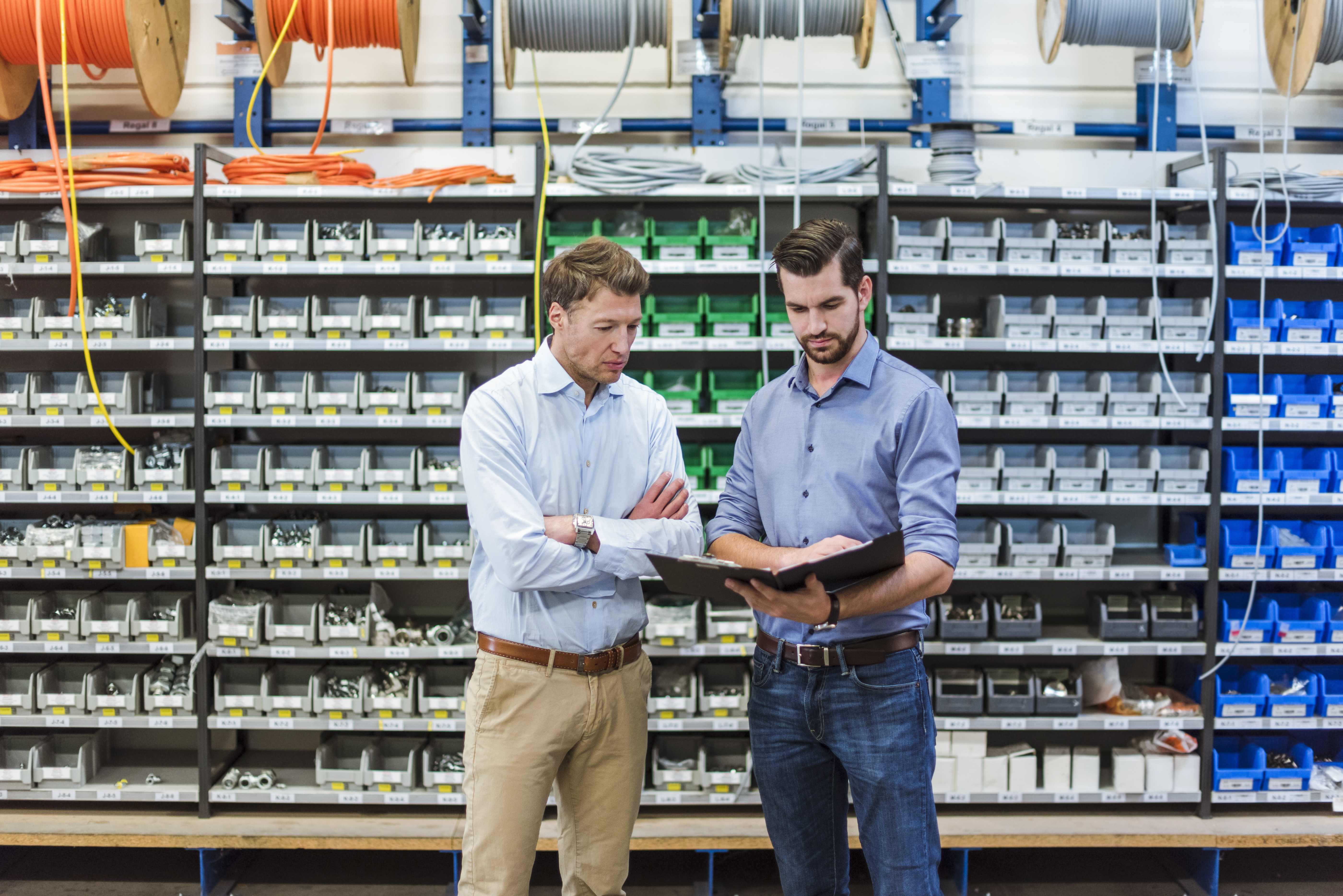 Two men standing in front of a vendor managed inventory solution of shelves and bins with production hardware parts