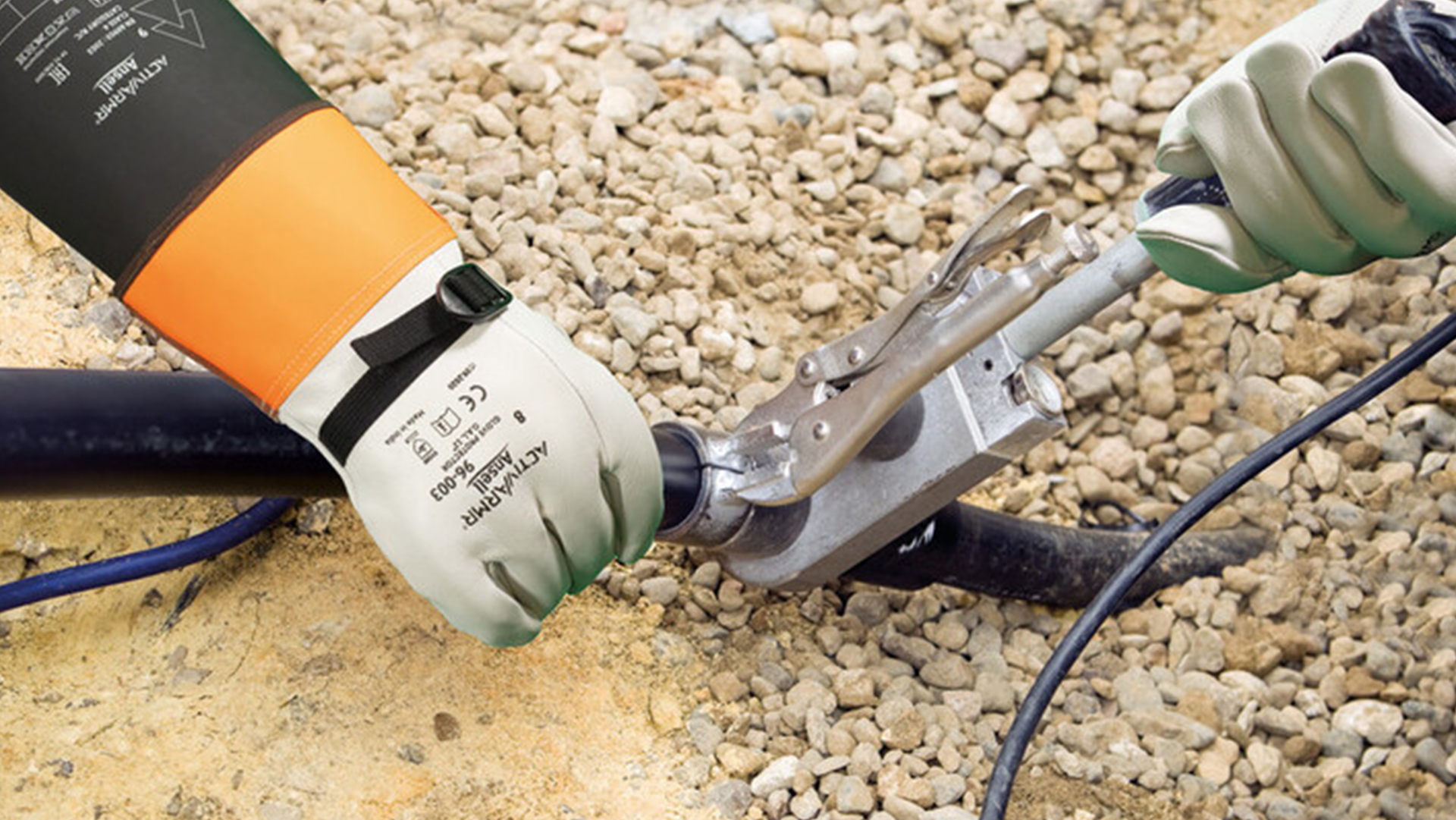 Electrical tools and equipment on gravel surface including orange and black device, metal clamp, and green insulator.