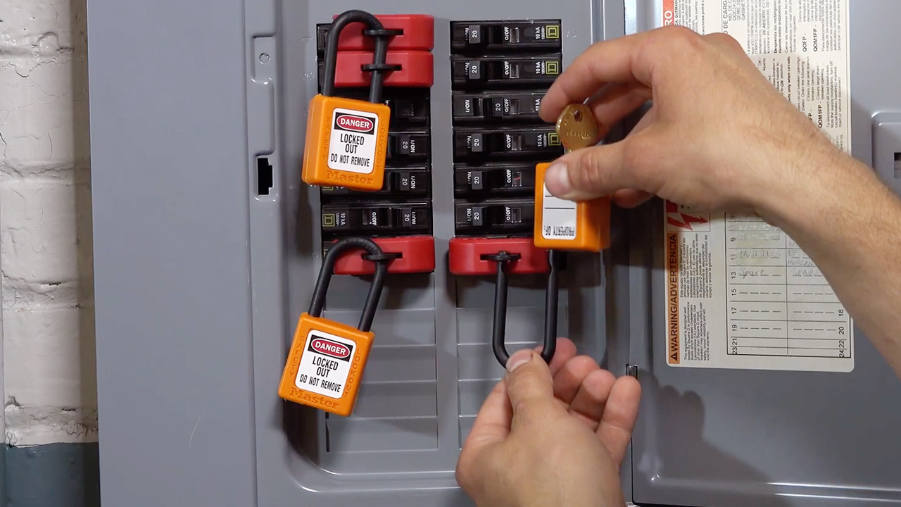 Hands using orange lockout tagout devices with danger labels on electrical panel circuit breakers for safety