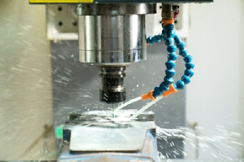 CNC machine spraying cutting fluid onto a metal workpiece to cool and lubricate.  