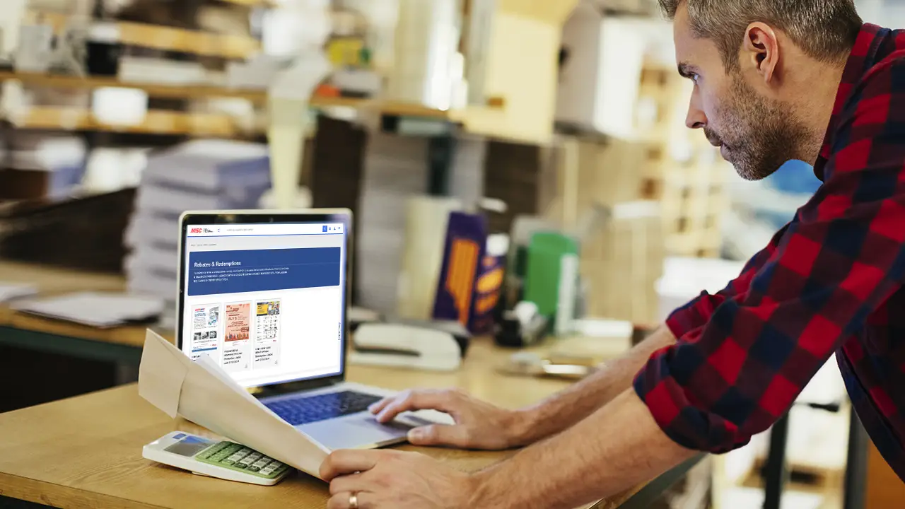 Man leaning over desk looking at laptop screen showing MSC's Rebates webpage