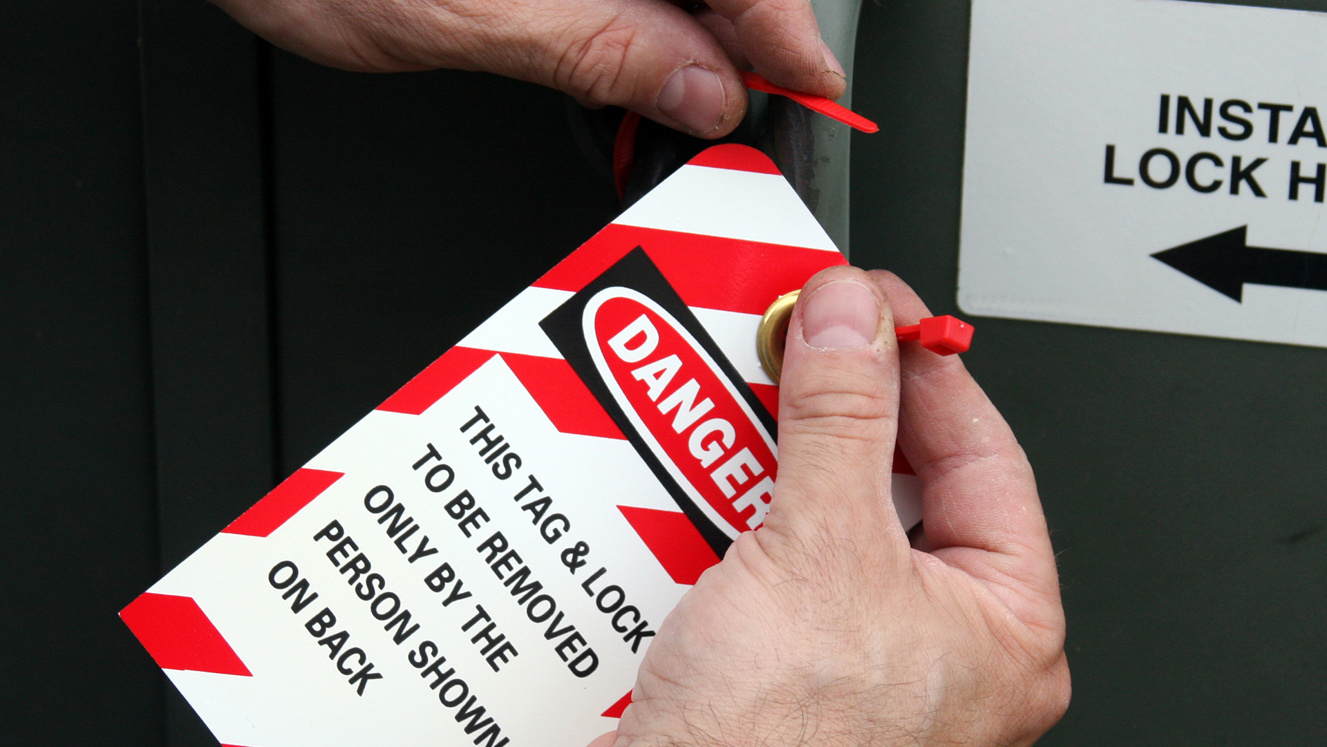 Hands attaching a red and white striped danger tag to equipment with lockout/tagout safety instructions visible.