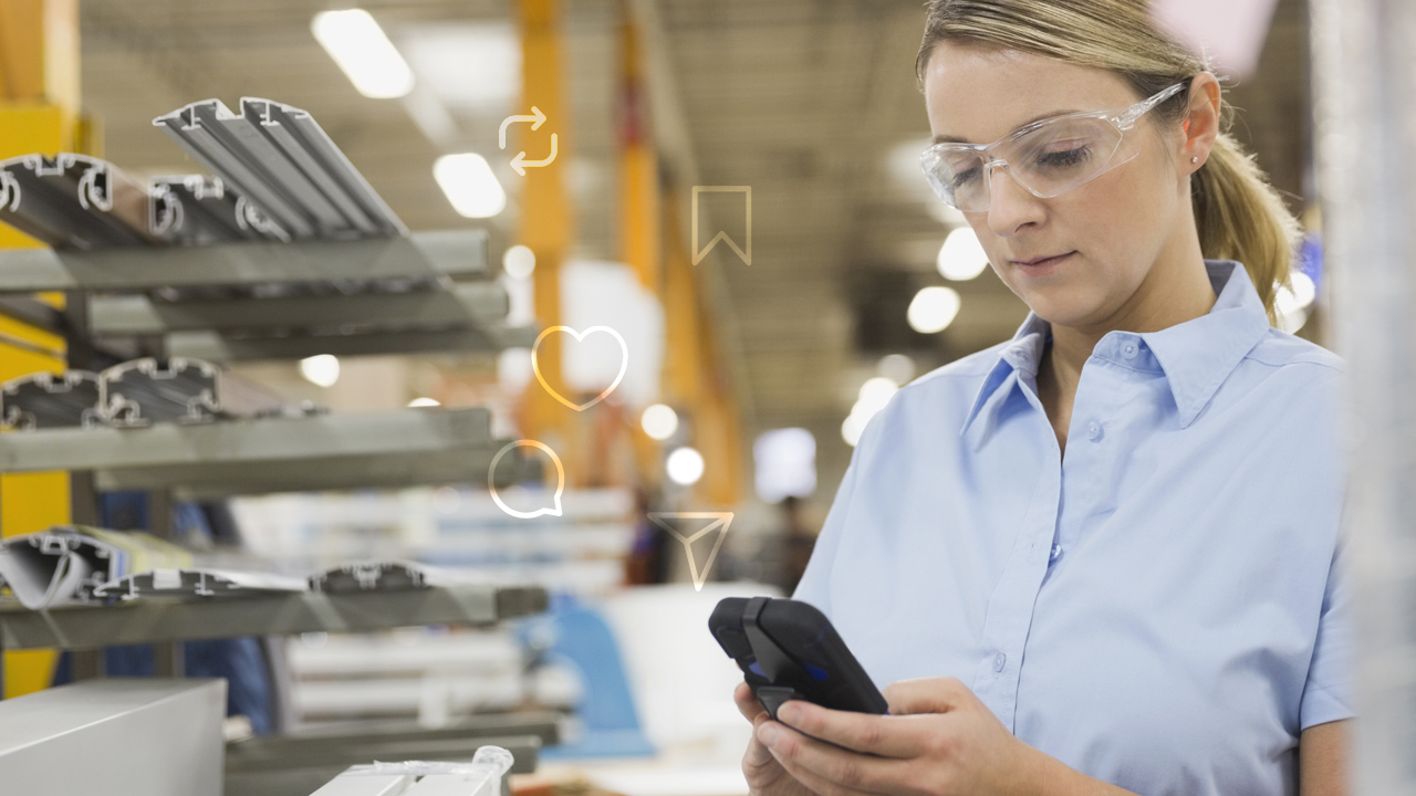 Female worker in safety goggles and blue shirt using smartphone in industrial warehouse setting