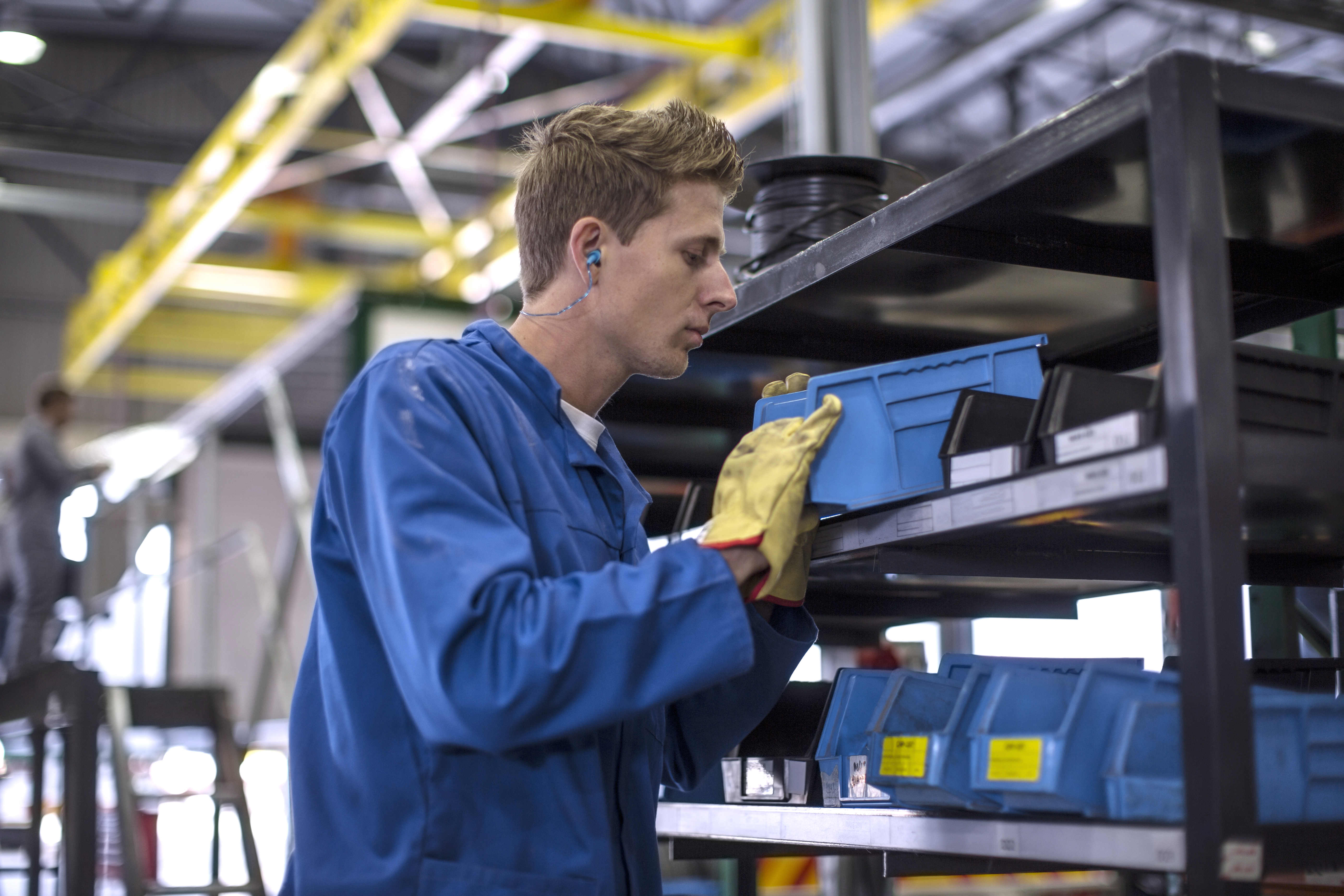 Man wearing gloves looking into a blue bucket of parts, as part of a vendor management inventory solution