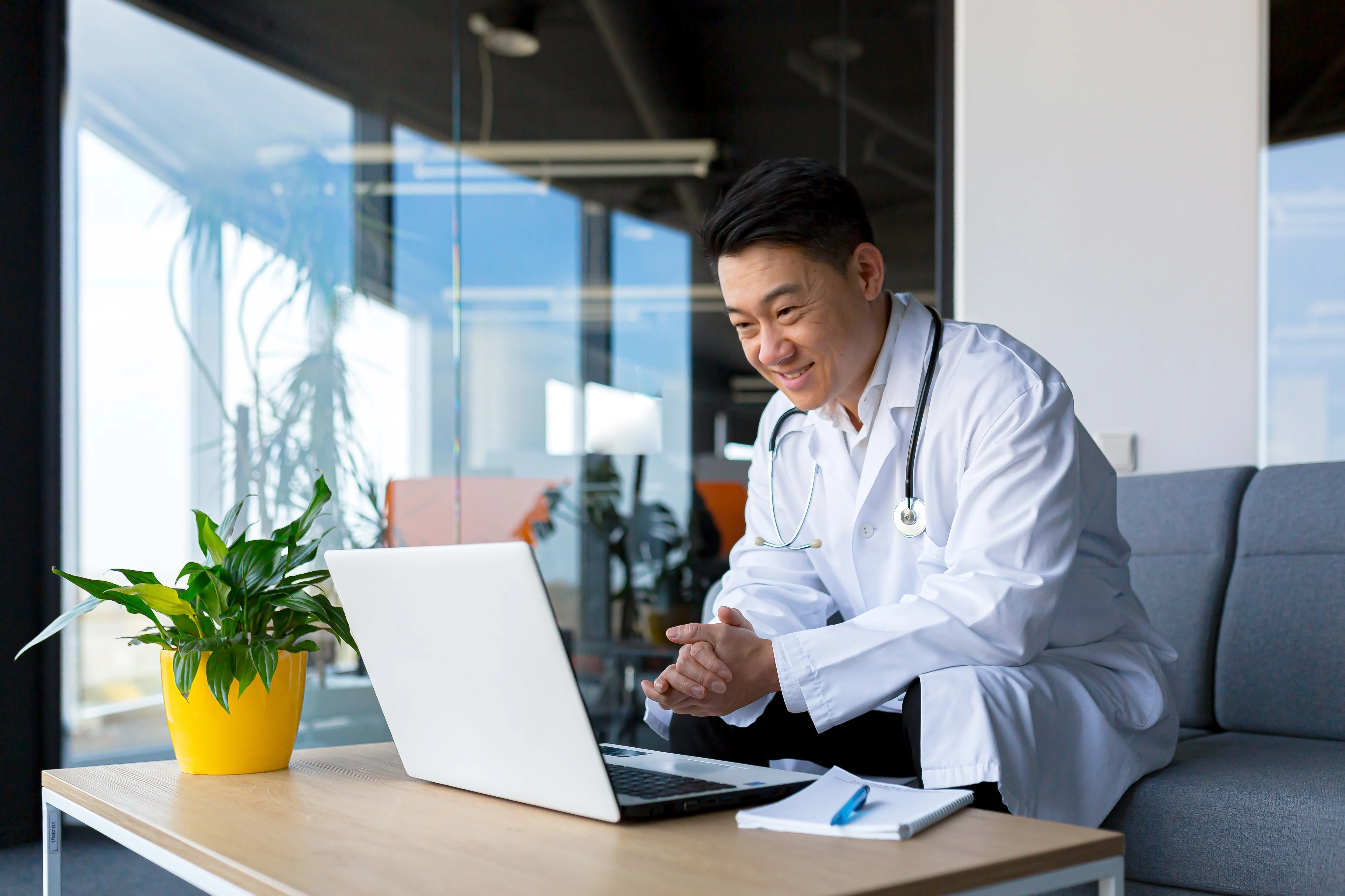 Asian male doctor looking at his laptop during a telehealth visit and smiling