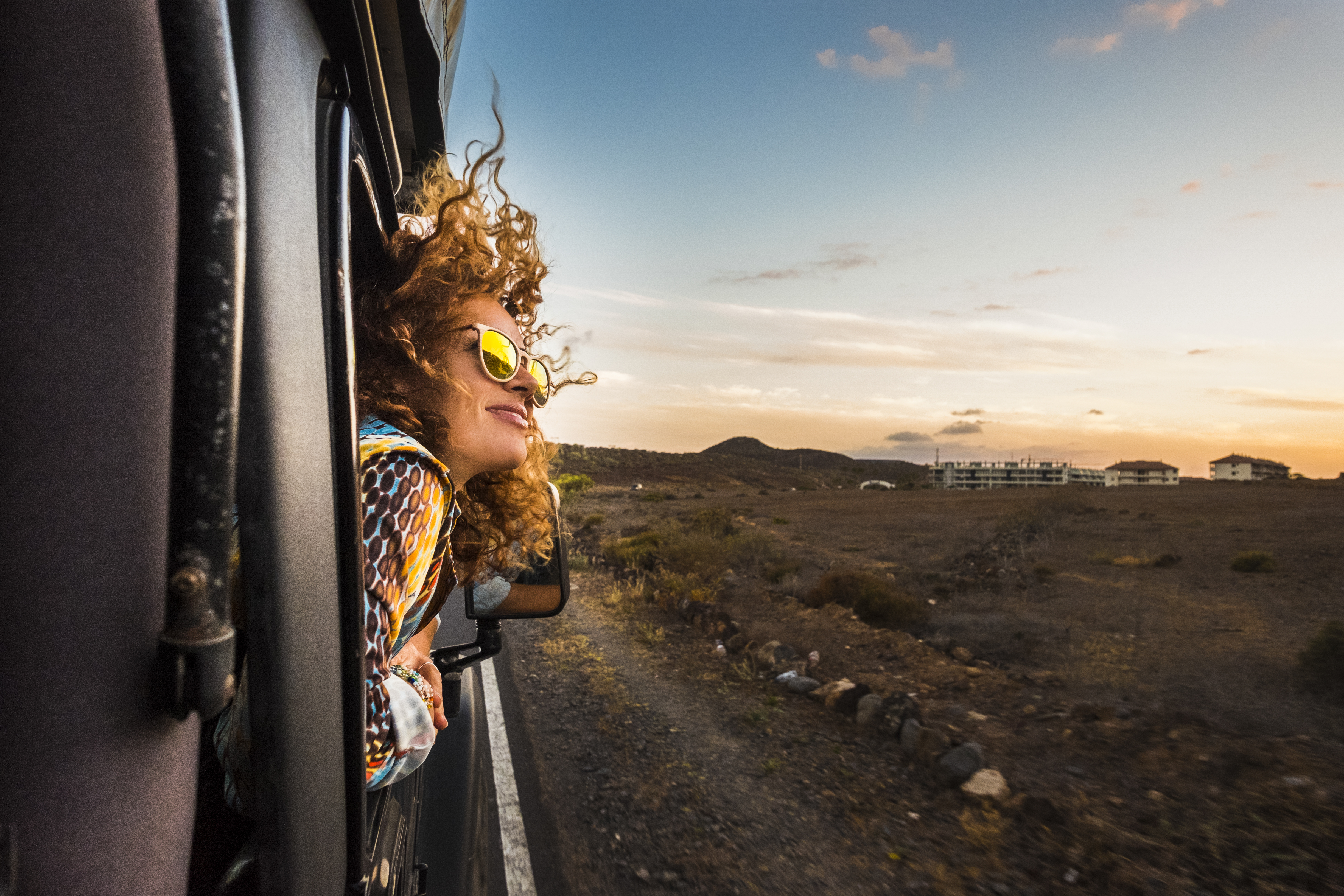 Woman leaning out of a train window during sunset looking happy