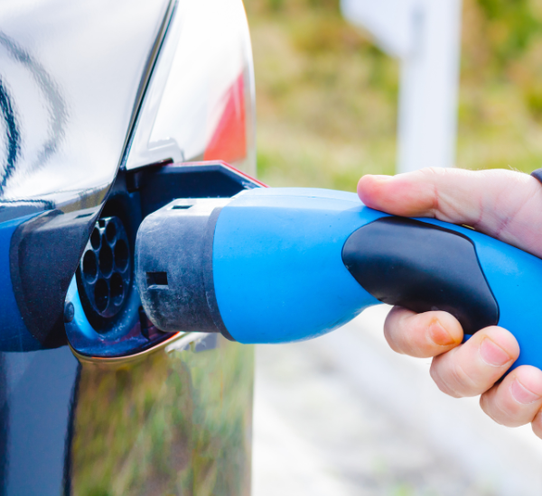 EV user holding an EV charger about to plug it into their car at city plumbing