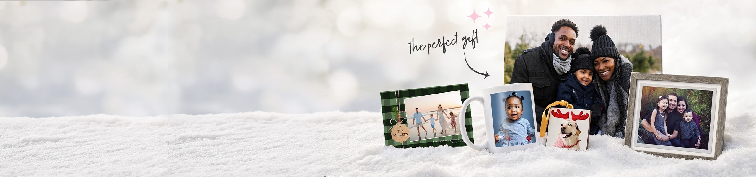 The perfect gift. Personalized gifts in the form of a photo book for a family, canvas print of a family, framed family photo, photo ornament of a dog and mug with a toddler on it on a blanket of snow.