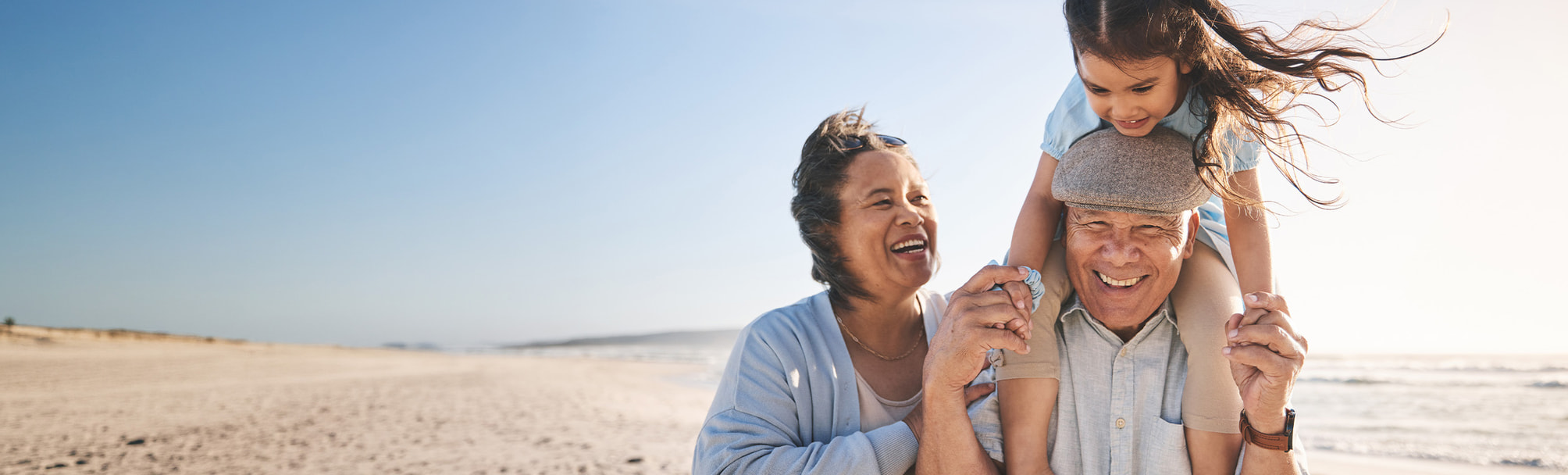 An older couple with a child on one of their shoulders smiles at the beach