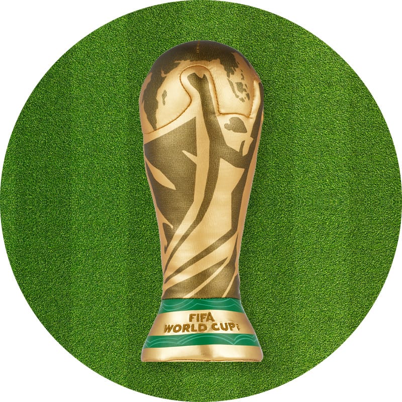 Gold FIFA World Cup trophy displayed upright on a green grass background with a green band at the base labeled "FIFA World Cup"