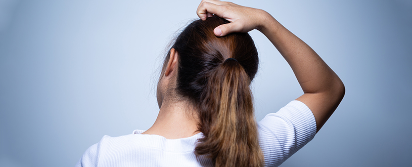 Woman facing away from the camera scratches at her itchy scalp.