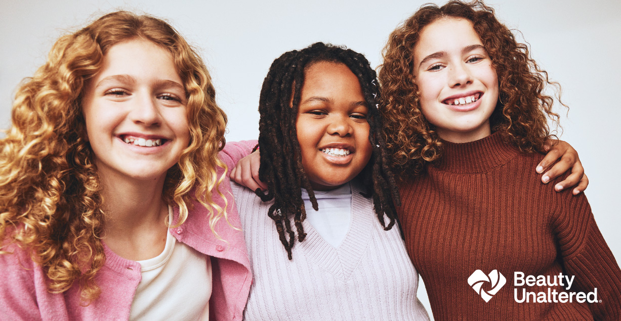 Beauty Mark + Beauty Unaltered® Three smiling teen girls with healthy looking hair & skin standing with arms around each other