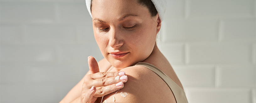 Woman applying lotion containing hyaluronic acid to dry skin on her upper arm.