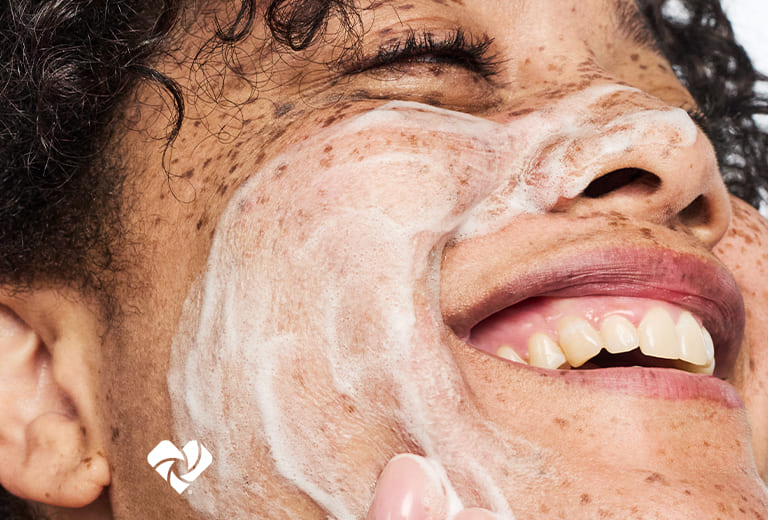 Close-up of a person looking upward with eyes closed and skin care lather on their face. Logo de Beauty Unaltered.