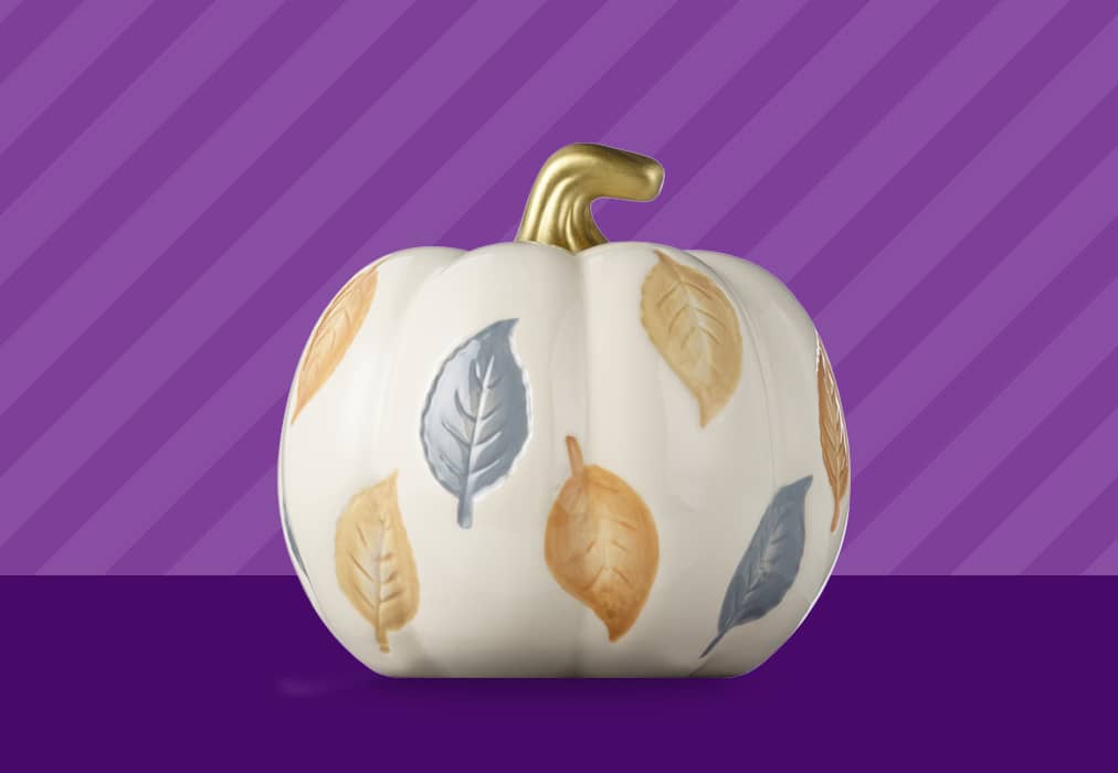 A decorative pumpkin with a gold stem and fall leaves over the surface.