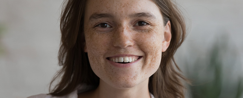 A woman with light brown hair with freckles all over her face smiling