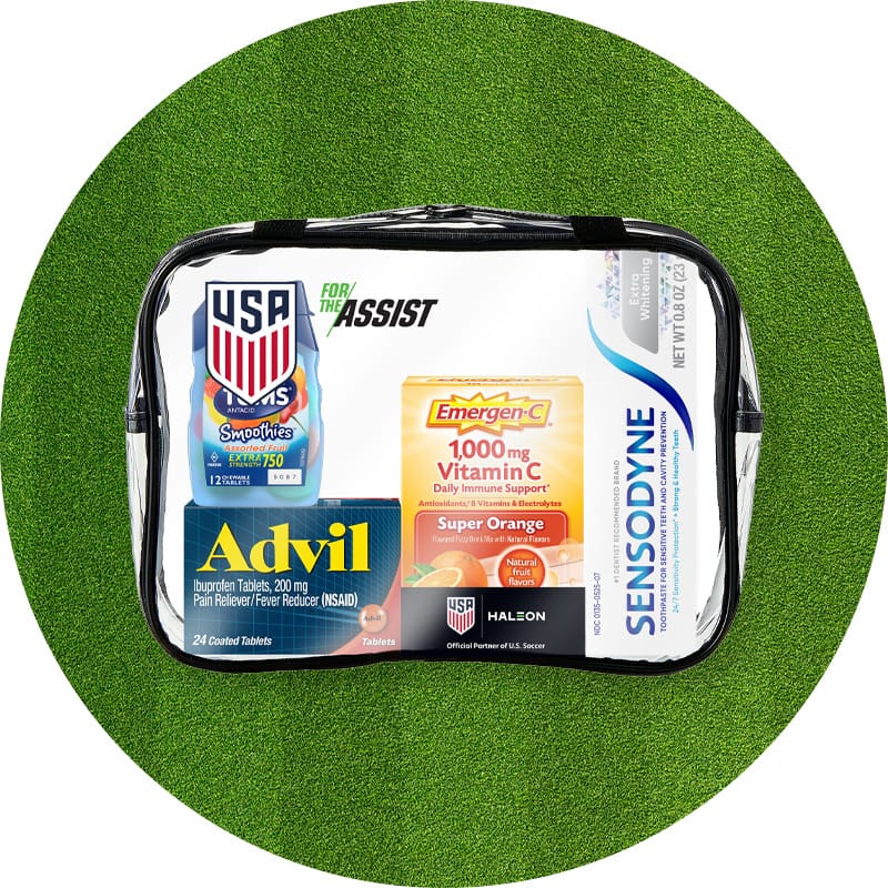 Soccer-themed clear travel bag with Advil, Emergen-C, Sensodyne toothpaste and Tums with a USA soccer logo and the words "for the assist" against a green grass background