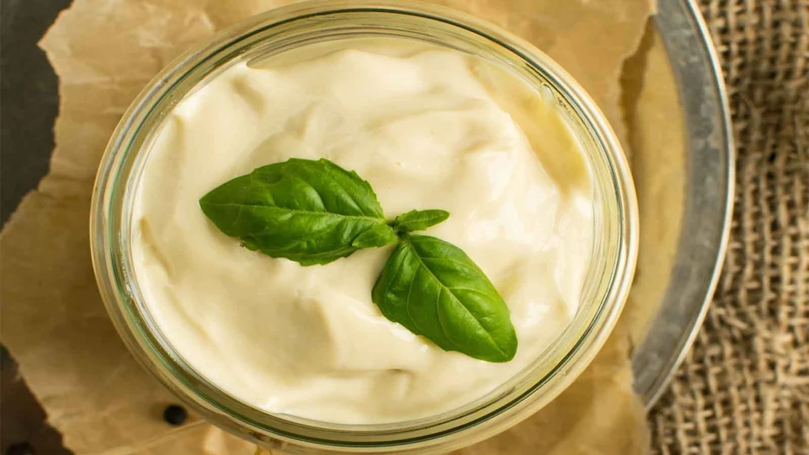 Pote de vidro circular visto de cima com maionese em seu interior e decoração com folhas de hortelã.