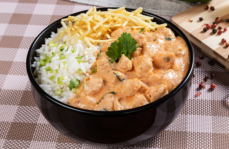 Strogonoff de frango em um bowl preto com batata palha e arroz.
