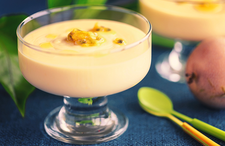 mousse de maracujá na taça de vidro em cima de uma mesa com plantas e talhares.