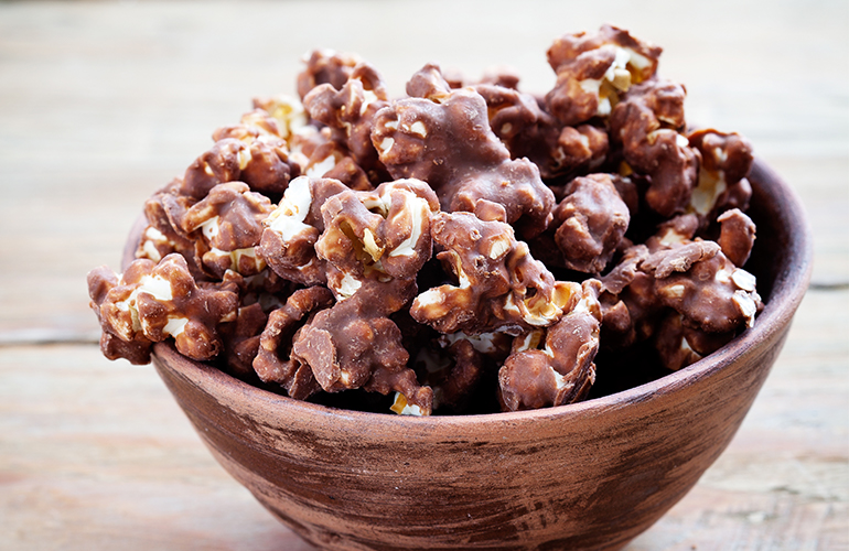 Pipoca doce com chocolate em um bowl marrom em cima de uma mesa de madeira.