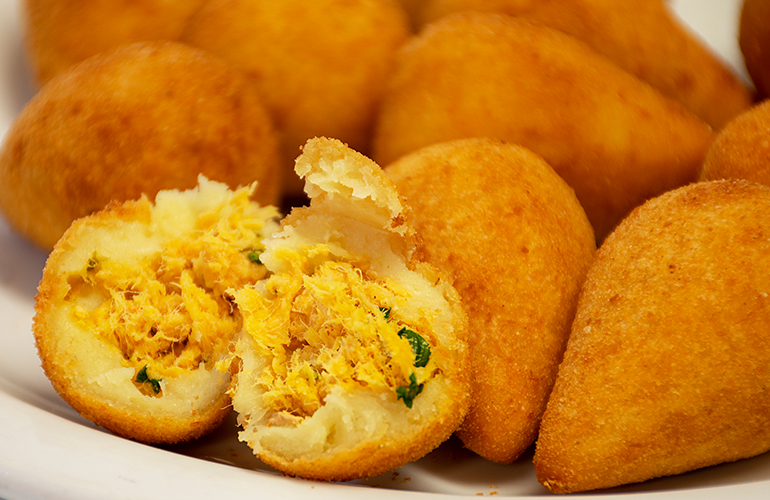 Prato com várias coxinhas de frango, sendo que uma delas está aberta no meio mostrando o recheio.