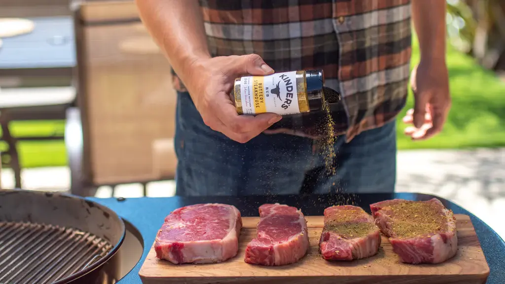 Hand seasoning four raw ny steaks on a cutting board